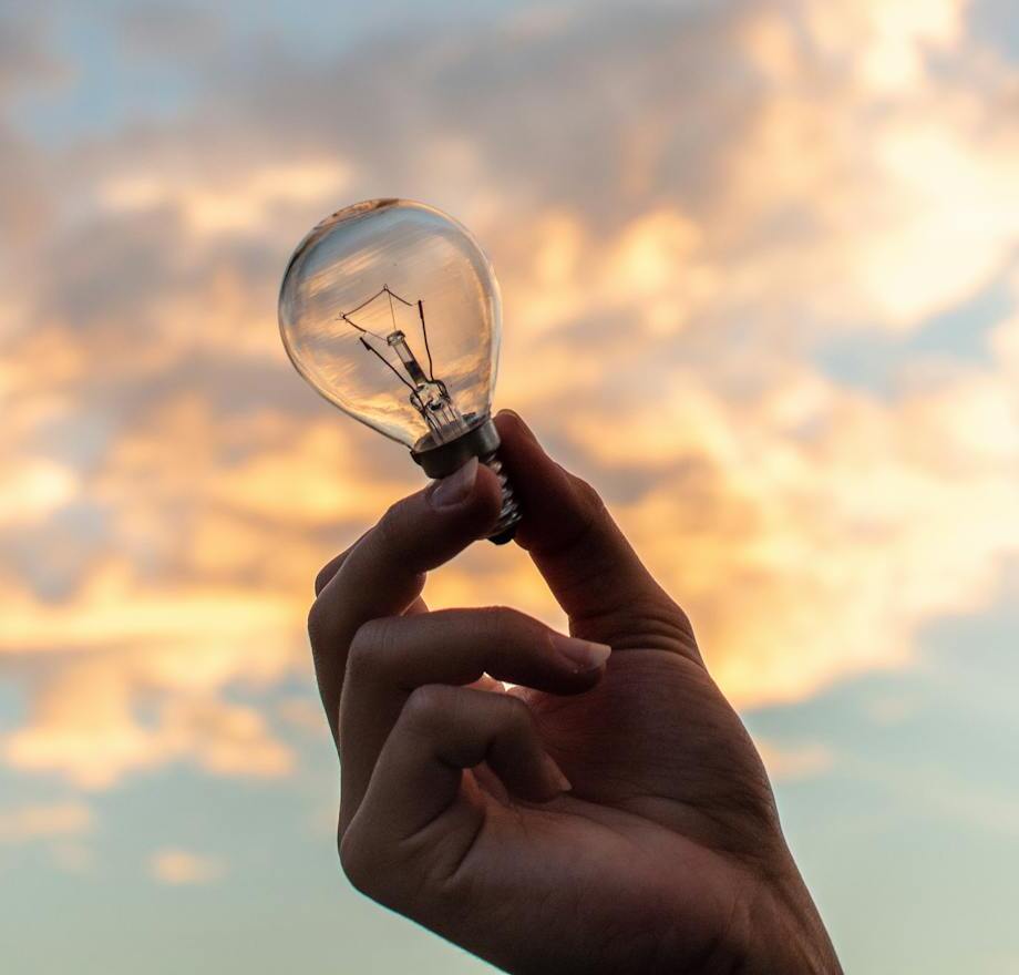 main tenant une ampoule avec un fond ensoleillé et nuageux